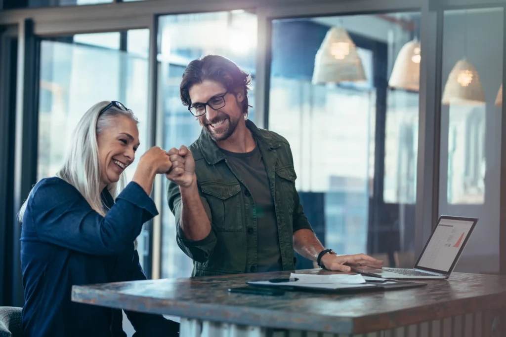 En glad kvinna och en man gör en fist bump på kontoret och framför sig er de ett digitalt onboardingprogram för chefer