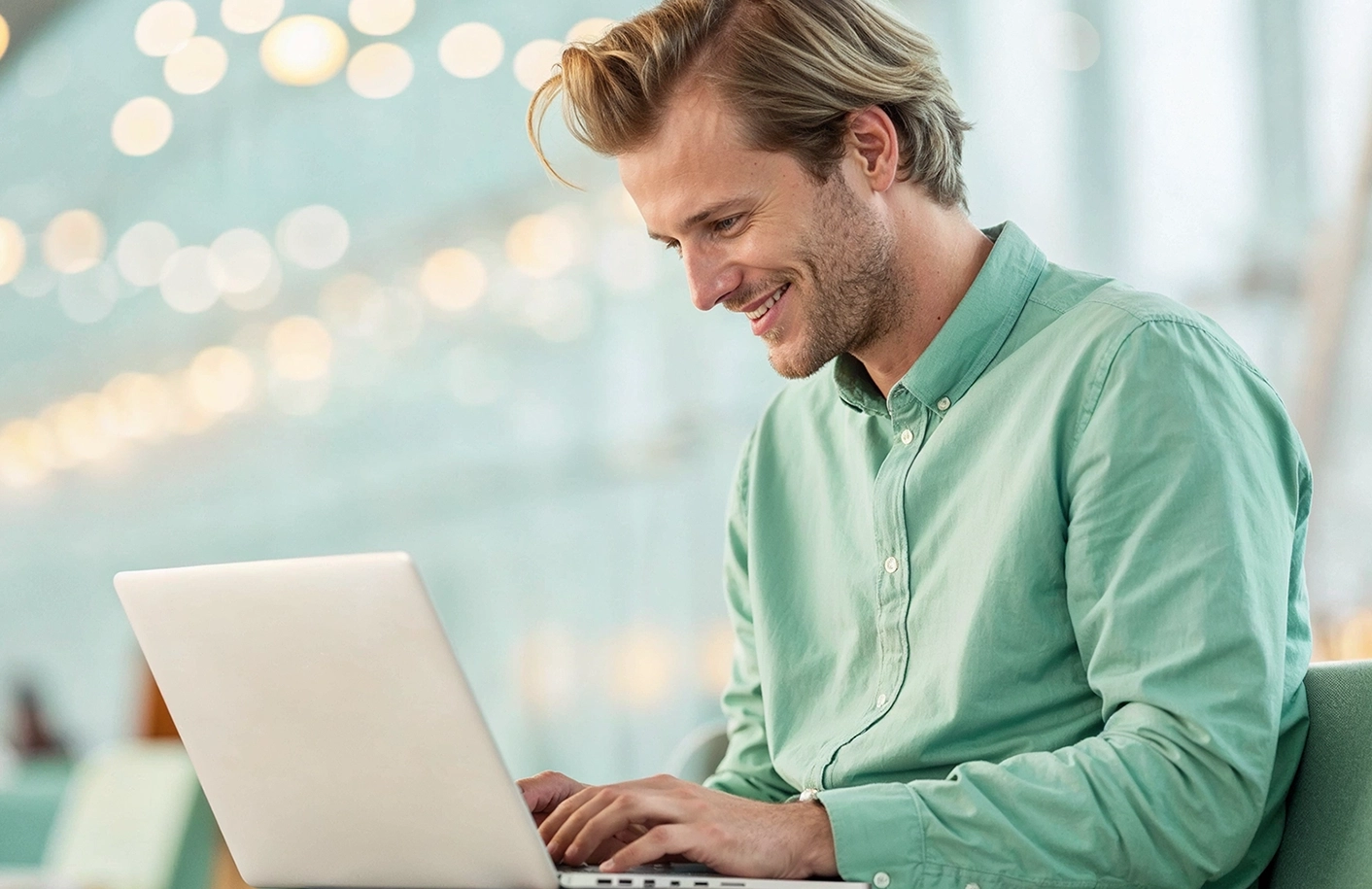 En glad man med en grön skjorta sitter med en laptop i knät